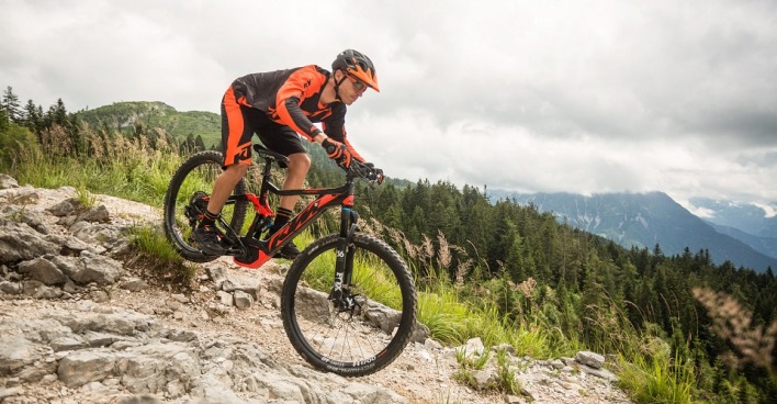 Mann mit Helm und Fahrradtrikot fährt mit einem E-Bike von KTM einen felsigen Berg hinunter.