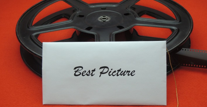 Eine schwarze Filmrolle auf einem roten Teppich an die ein weißer Briefumschlag mit der Beschriftung Best Picture angelehnt ist