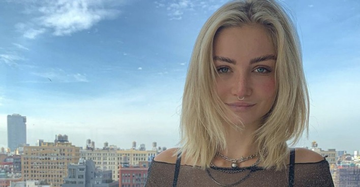Junge blonde Frau mit Nasenpiercing vor der Kulisse New Yorks und blauem Himmel