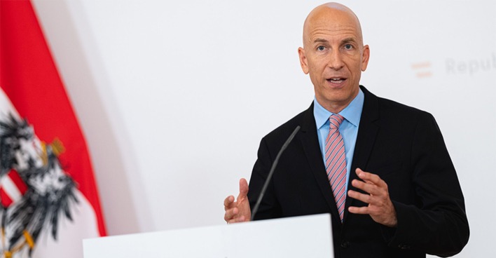 Kocher erklärt bei der Pressekonferent mit österreichischer Fahne im Hintergrund, die neuen Arbeitsmodelle