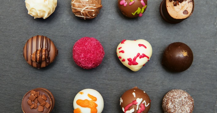 12 unterschiedliche bunte Pralinen geometrisch angeordnet auf einem Tisch