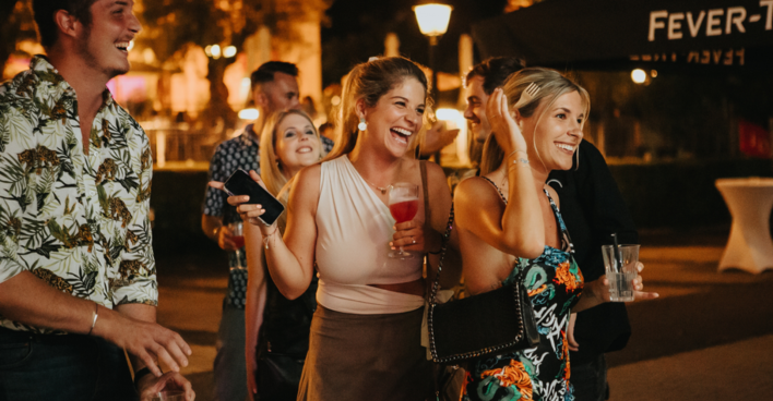 Nacht, zwei Frauen die lachen und Drinks in der Hand halten.