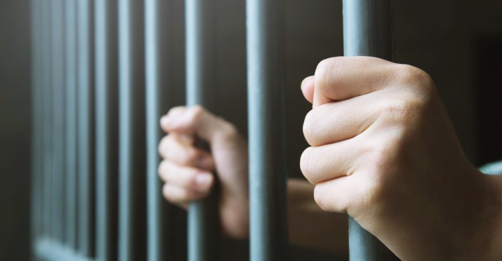 Zwei Hände, die zwei Gitterstäbe einer Gefängnistür umschließen