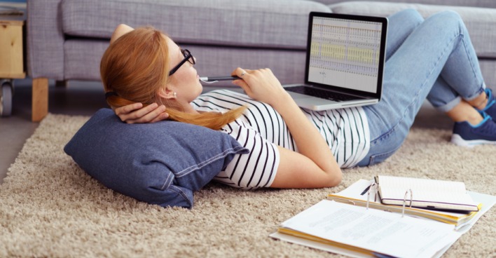 Junge Frau mit Notebook auf dem Schoß lernt im Liegen | Credit: iStock.com/stockfour