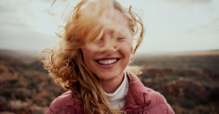 Stürmischer Wind fährt einer glücklichen jungen, rothaarigen Frau durchs lange Haar | Credit: iStock.com/Lyndon Stratford