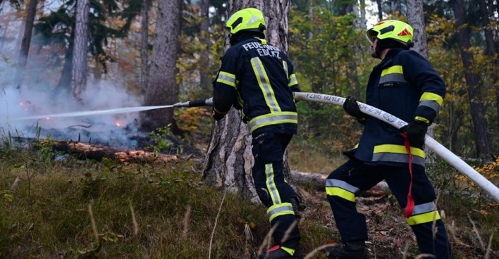 Zwei Feuerwehrmänner löschen einen Glutherd im Wald.