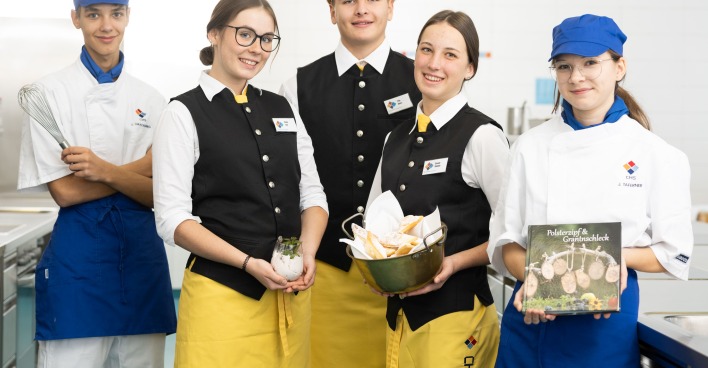 Schüler des CHS-Villach in eleganter Gastro-Montur halten ein Kochbuch und einen Brotkorb in die Kamera