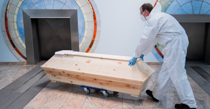 Mann in Schutzanzug schiebt Sarg Richtung Öffnung des Ofens