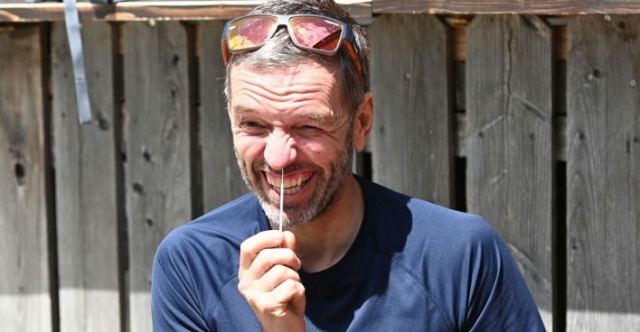 Herbert Kickl macht einen Corona-Selbstest. Er fährt mit einem Wattestäbchen in die Nase und zieht eine Grimasse. Kickl trägt eine Sonnenbrille am Kopf und sitzt vor einer Holzwand. Das Foto ist bei einer Wanderung entstanden.