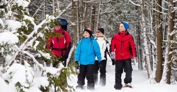 Eine Familie stapft in Schneeschuhen durch ein schneebedecktes Waldstück