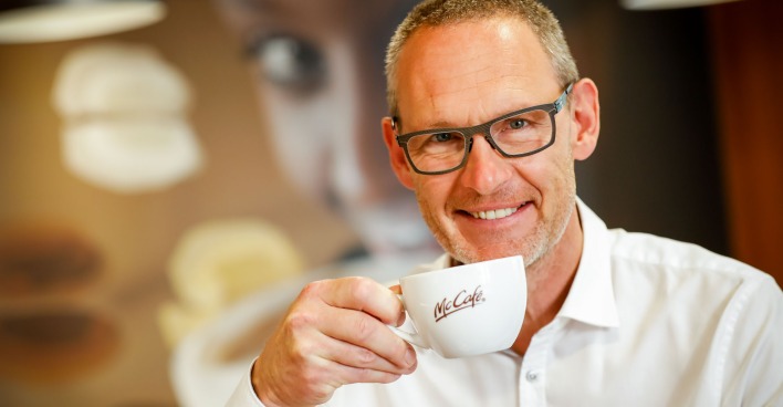 Rudolf Ringhofer führt eine Kaffeetasse mit McCafé-Logo zu seinem Mund