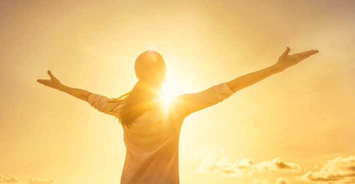 Mit seitlich ausgestreckten Armen blickt eine junge Frau der Sonne entgegen | Credit: iStock.com/kieferpix