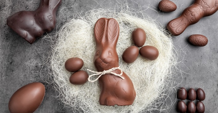 Mehrere Schokoosterhasen und Schokoeier in einem Nest aus weißer Wolle