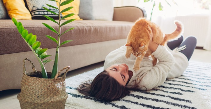 Frau liegt mit ihrer Katze auf dem Teppich ihres gemütlichen Wohnzimmers | Credit: iStock.com/Maryviolet
