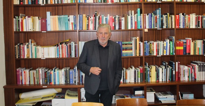 Der Obmann des KHD, Andreas Mölzer, steht vor einem mehrreihigen Bücherregal mit unzähligen Büchern