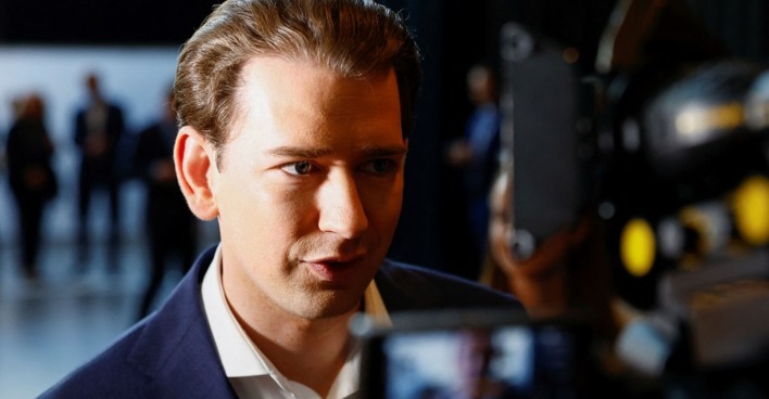 Sebastian Kurz im Halbporträt, sein Gesicht ist nur von einer Seite beleuchtet. Eine Kamera ist auf ihn gerichtet, er gibt ein Interview.