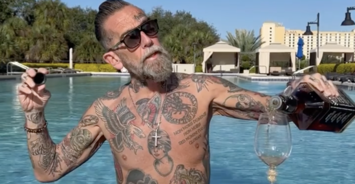 Roland Ludomirska mit nackten Oberkörper, voll tättowiert und einer Flasche Jack Daniels in einem Pool