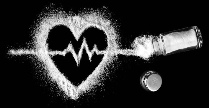 Ein umgekippter Salzstreuer mit dessen Inhalt ein Herz samt EKG Linie auf einen schwarzen Hintergrund gemalt wurde