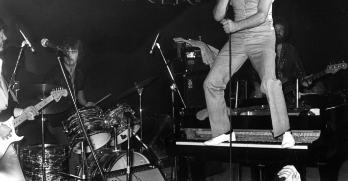 Rock‘n‘Roll-Legende Jerry Lee Lewis auf einem Klavier stehend