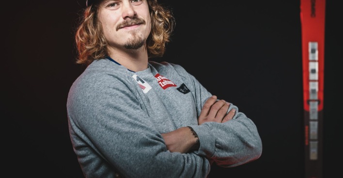 Manuel Feller, der mit verschränkten Armen und einer Baseballmütze auf dem Kopf vor seinen Rennski steht.