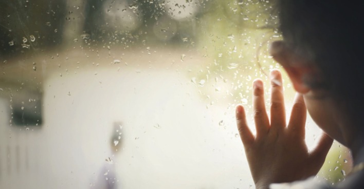 Kind hat Hand am Fenster und schaut raus