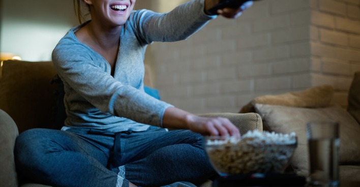 Frau schaltet mit Fernbedienung Fernseher ein