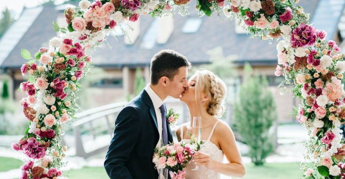 Ein Brautpaar beim Hochzeitskuss unter einem Blumenbogen