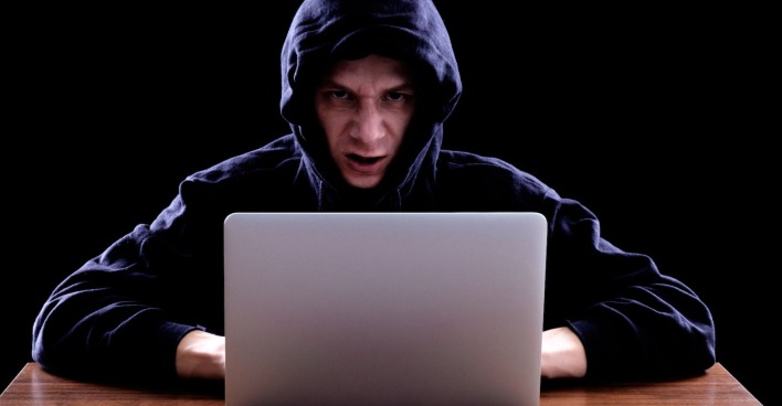Mann mit schwarzem Kapuzenpullover vor einem Laptop| Credit: iStock.com/filistimlyanin