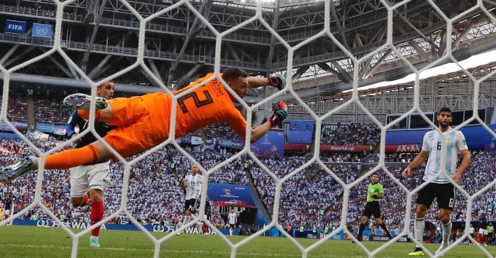 Der argentinische Fußball-Torhüter in einem orangen Dress, der - durch die Maschen des Tornetzes fotografiert -, durch die Luft hechtet