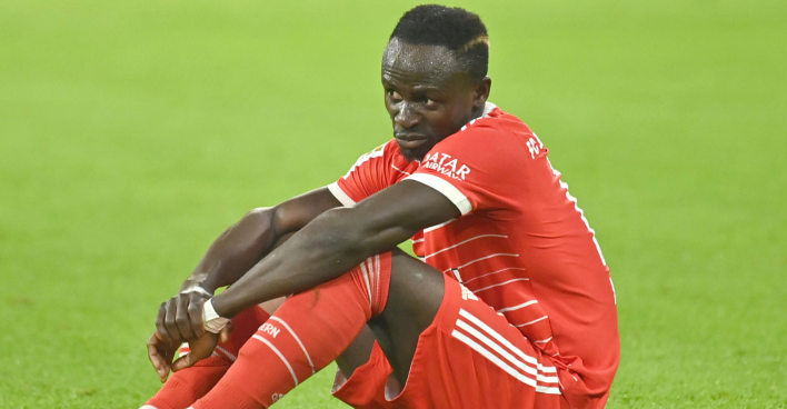 Sadio Mané, der im Dress des FC Bayern München mit einem nachdenklichen Gesichtsausdruck auf dem Spielfeld sitzt.