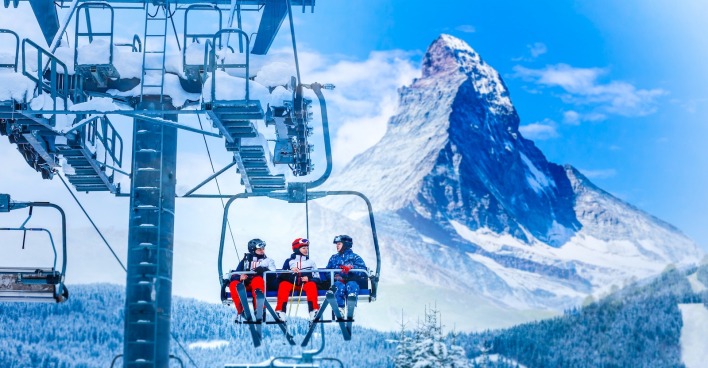 Drei Menschen fahren in Zermatt mit dem Sessellift. | Credit: iStock.com/Sinenkiy