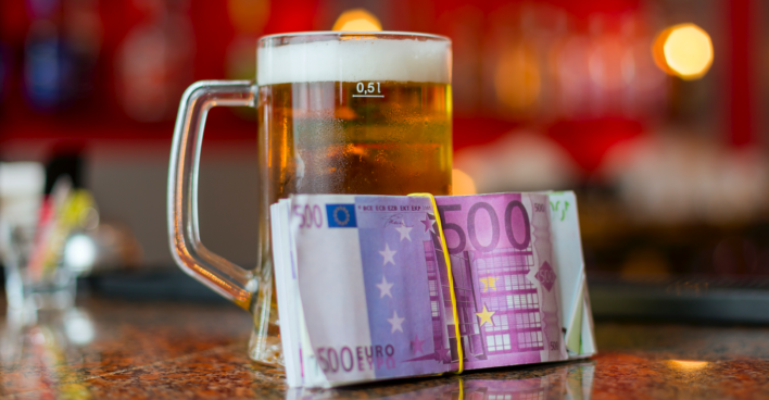 Ein Glas Bier auf einer Theke, an dem ein Bündel 500-Euro-Scheine lehnt