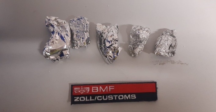 Vier kleine Päckchen aus Aluminiumfolie, darunter ein Schild mit der Beschriftung "BMF / Zoll / Customs"