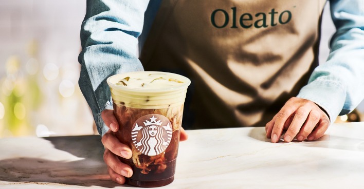 Eine Hand reicht einen Becher mit Oleato Golden Foam in einem Becher mit Starbucks Logo über den Tresen