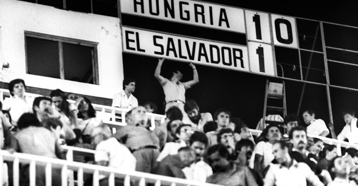 Schwarz-Weiß-Aufnahme der Publikumsränge in der Partie Ungarn - El Salvador. Im Hintergrund ist die Anzeigentafel zu sehen, die das Resultat 10:1 aufweist