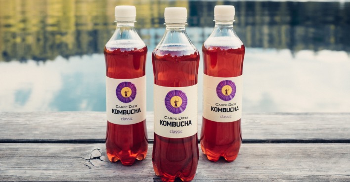 Drei Flaschen Kombucha vor einem See.