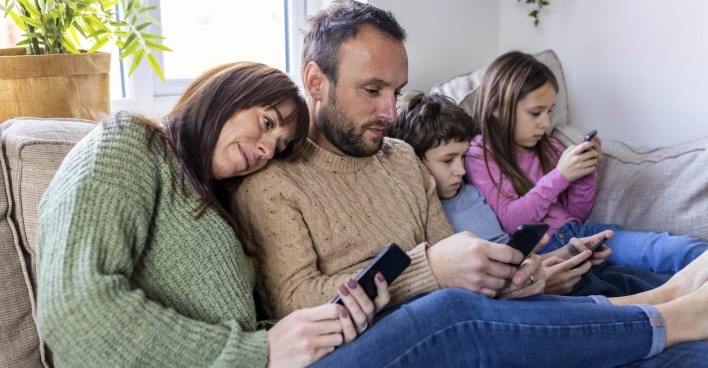Mutter, Vater und zwei Kinder sitzen auf dem Sofa und schauen jeder in ein Smartphone