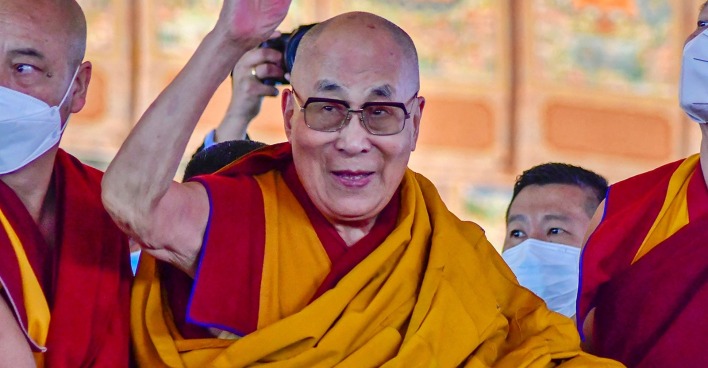 Der Dalalai-Lama umgeben von Gefolgsleuten lacht und winkt