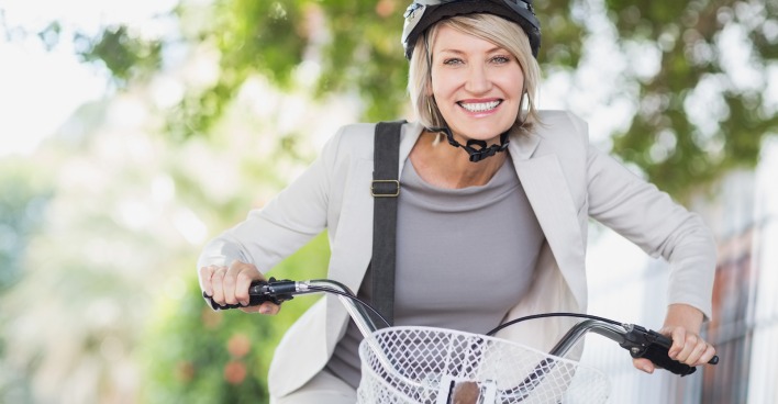 lächelnde Frau mit weißen Business-Outfit und Helm am Fahrrad | Credit: iStock.com/Wavebreakmedia
