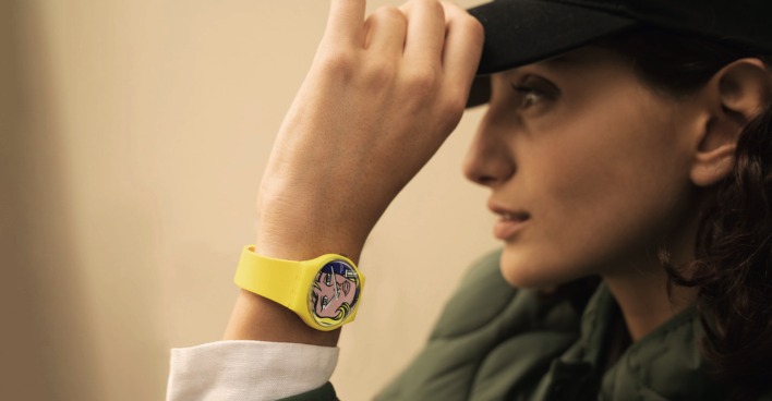 Model trägt eine Capy, grüne Jacke und eine gelbe Swatch Uhr aus der Swatch Art Journey Kollektion