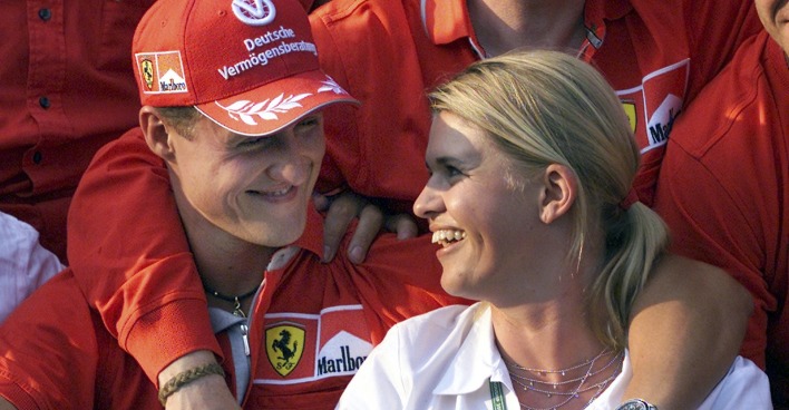 Michael und Corinna Schumacher sitzen Arm in Arm nebeneinander und schauen sich verliebt an.