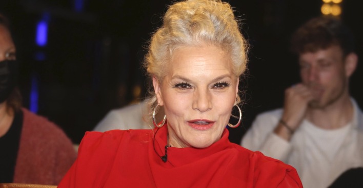 Ina Müller in einem roten Kleid mit großen Ohrringen.