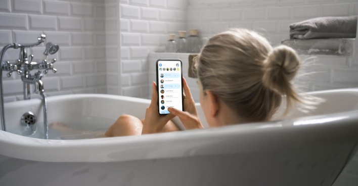 Frau liegt mit Handy in der Badewanne