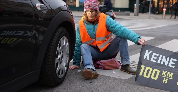 Eine Klima-Kleberin sitzt direkt vor einem Auto. (SYMBOLBILD)