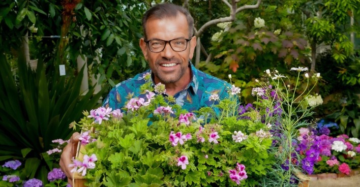 Karl Ploberger hält im Garten eine Holzkiste mit blühenden Sommerblumen | Credit: ORF/Roman Zach-Kiesling