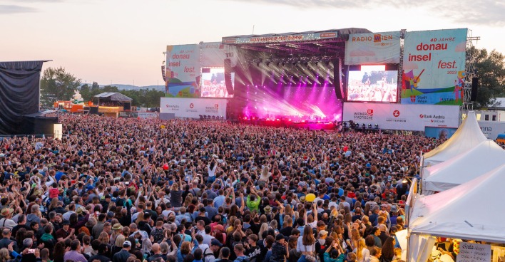 Eine große Menge Zuseher steht vor der Hauptbühne am Donauinselfest. Auf der Bühne eine Show