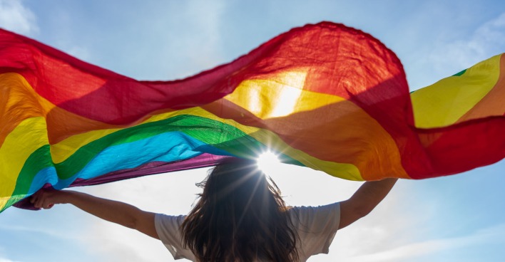Frau hält Regenbogenflagge hoch in die Luft