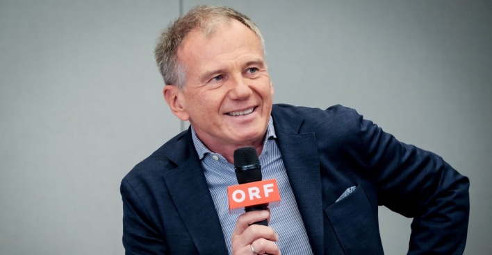 Armin Wolf ist im Gespräch, er lächelt und hält ein ORF-Mikrofon in der Hand.