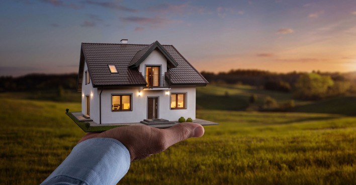 Mann hält beleuchtetes Haus in Miniaturform in seiner Hand | Credit: iStock.com/Nastco