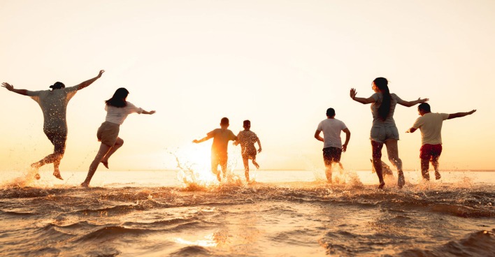 Gruppe junger fröhlicher Menschen läuft ins Meer | Credit: iStock.com/molchanovdmitry